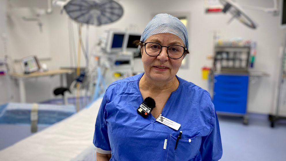 En kvinna med hårnät och blå sjukhuskläder står i en vit operationssal