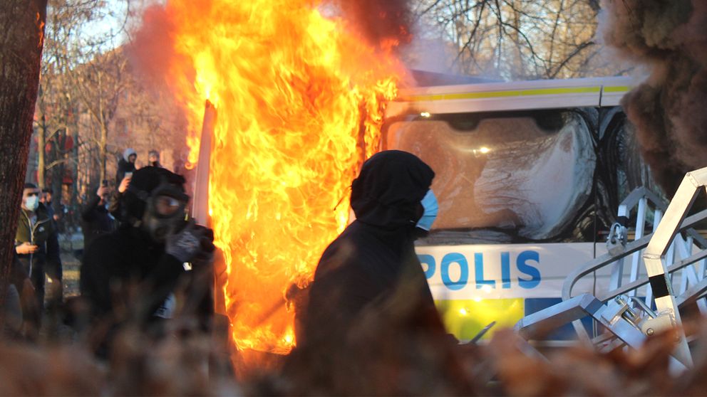 Maskerade personer framför brinnande polisbil