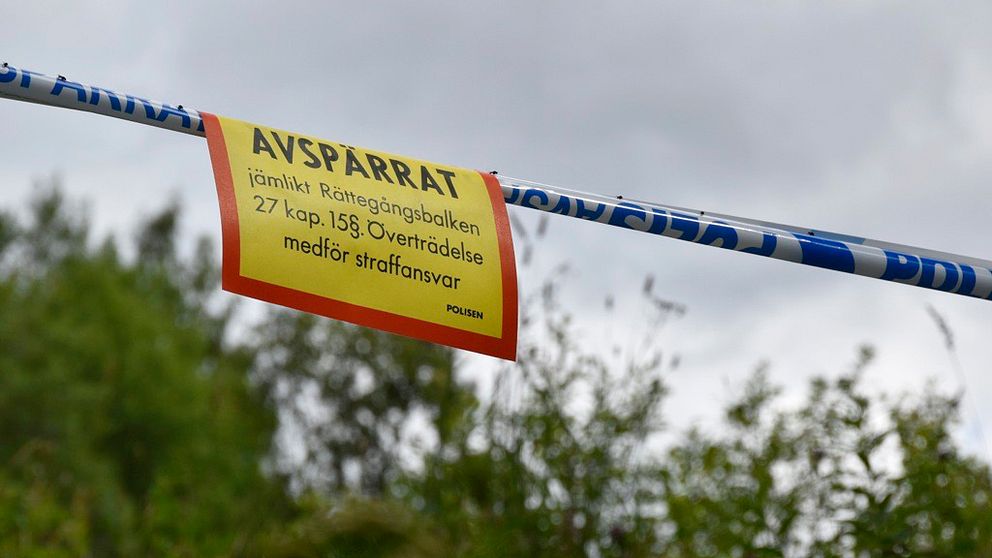 polistejp och skylt om avspärrat område, buskage och himmel bakom