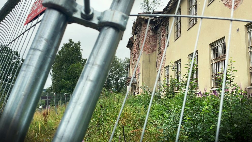 Bild på en gul förfallen byggnad genom kravallstaket.
