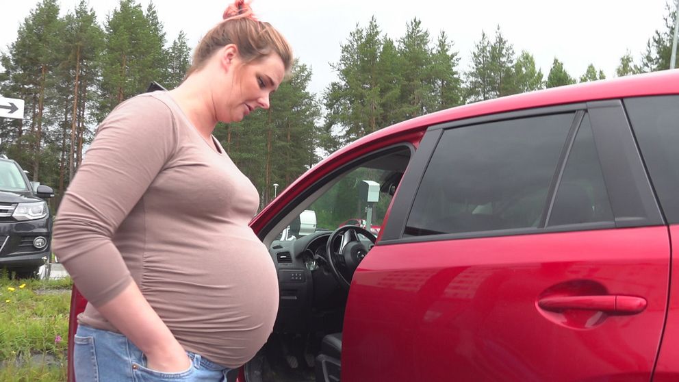 Gravid kvinna står framför en röd bil i Lycksele