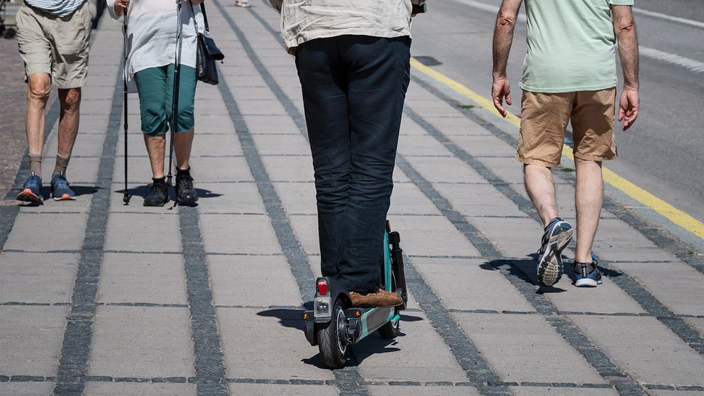 En man åker elsparkcykel på trottoar.