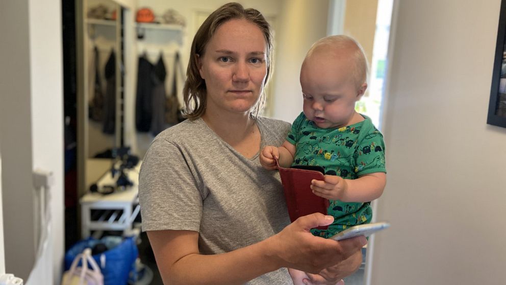 Amelia Luukkonen står med sin ettårige son Elton på armen och håller också i sin mobiltelefon. Hon kollar in i kameran.