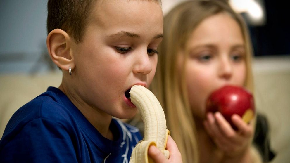 Barn sitter och äter frukt.