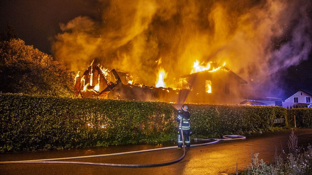 brandman sprutar vatten över en häck på ett hus som är helt övertänt