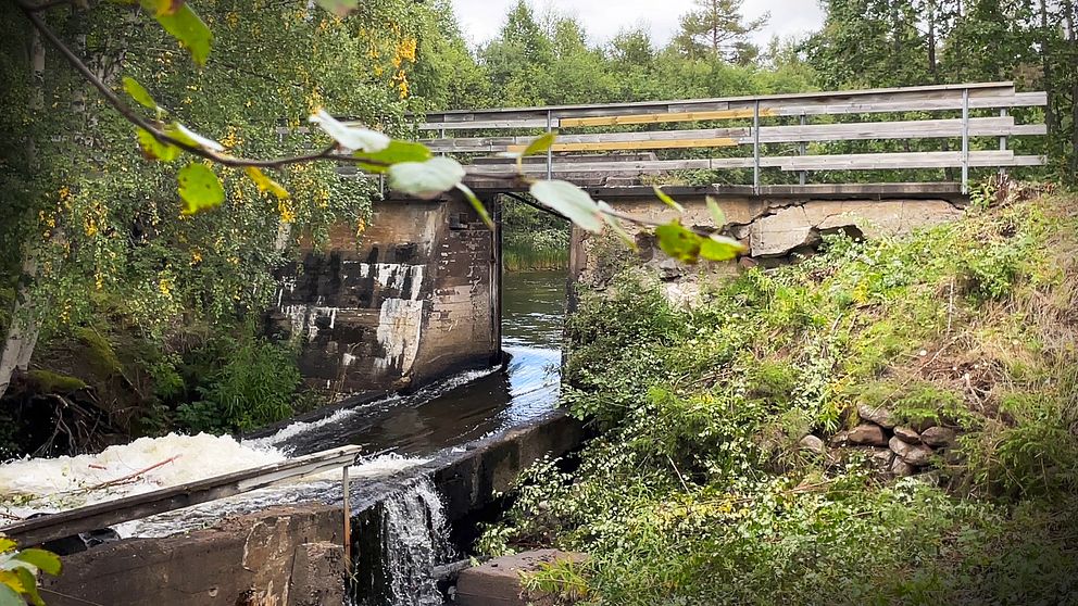 En bild på en sliten kraftverksdam, man kan skymta en slags bro som går över ett vattendrag.