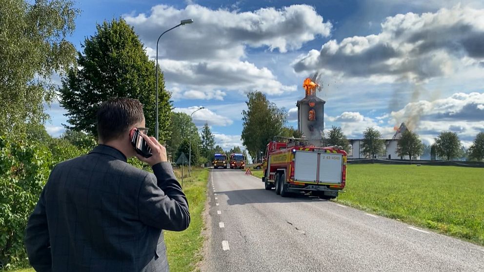 Man med mobiltelefon mot örat tittar mot en brandbil och en brinnande kyrka.