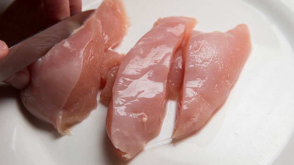 Råa kycklingfiléer blir skurna i bitar av en hand med kniv.