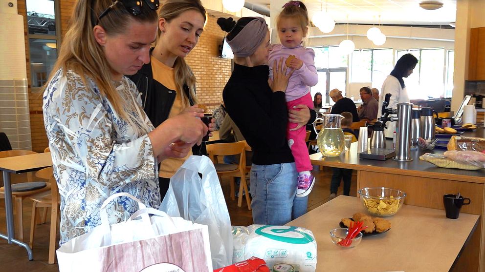 Tre ukrainska kvinnor på Frälsningsarmén i Halmstad kollar på blöjor och barnmat, en av dem håller ett litet barn.