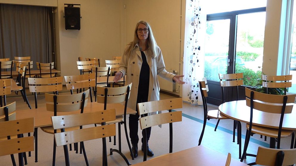 Erika Tor Rundblad står i en skolmatsal bland bord och stolar. Väggarna i bakgrunden är kala.