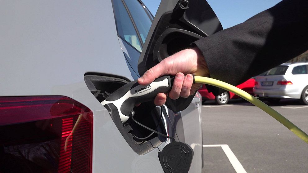 En person håller i en snabbladdarkontakt för elbil och stoppar i den i bilen.