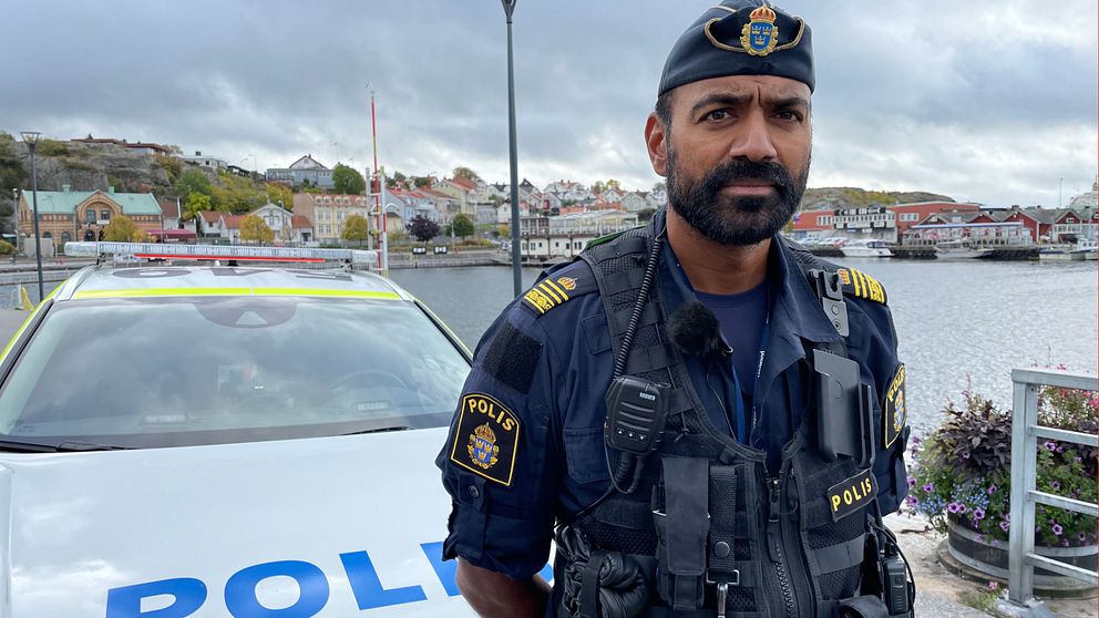 Medelålders man med mörkt, ganska kort skägg, ståendes framför en polisbil i Strömstads hamn. Han bär kortärmad mörkblå polisuniform och en polismössa.