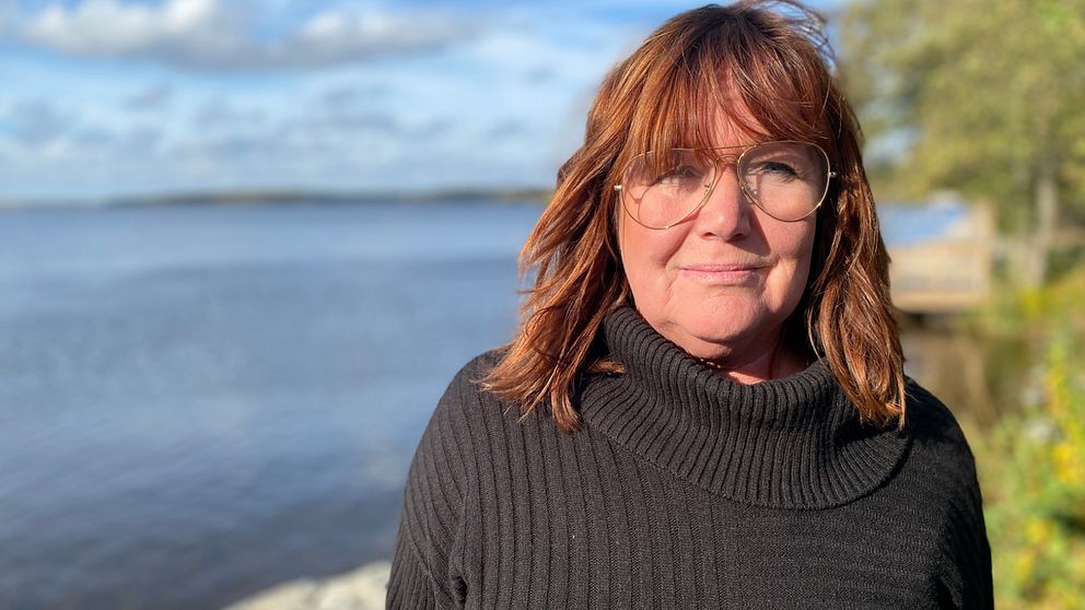 Bild på Eskilstunas stadsbyggnadsnämnds ordförande, Sarita Hotti (S). Hon har rött hår med pannlugg. Hon har på sig en svart polotröja och pilotglasögon. I bakgrunden skymtar Mälarem och grön växtlighet.