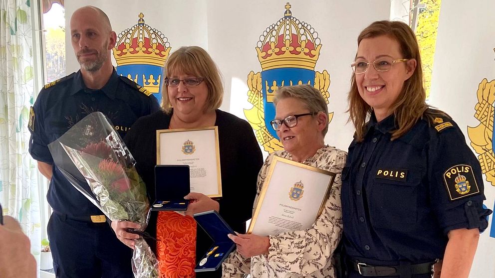 Två poliser och Anneli Gustafsson och Marie Ridvall ler med diplom och blomsterbuketter i samband med utdelningen av medborgarmedaljer för insatsen vid branden i en radhuslänga i Bergvik.