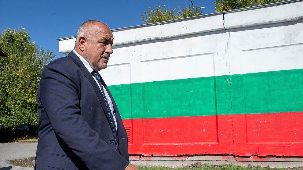 Boyko Borisov går förbi en mur med en stor bulgarisk flagga påmålad.