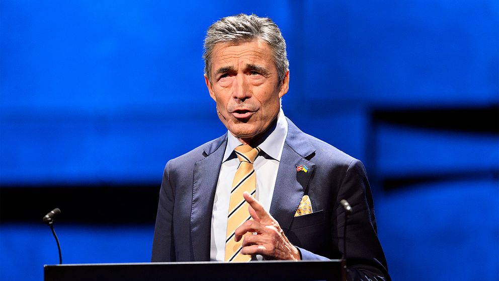 Anders Fogh Rasmussen står och håller tal mot en blå bakgrund.