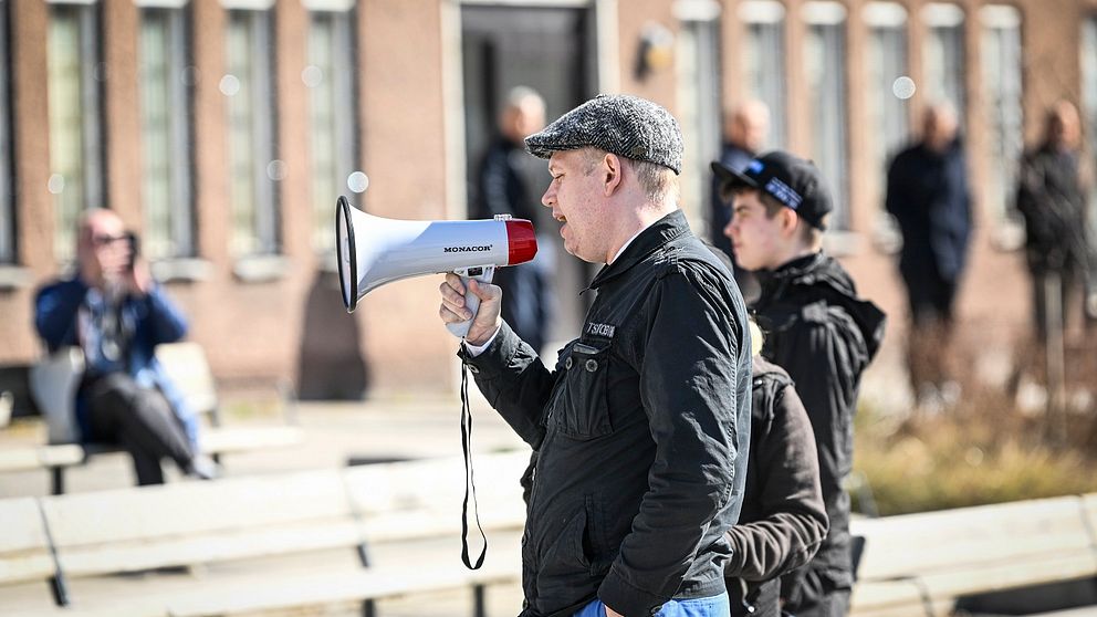 Man med keps håller tal till en folksamling.