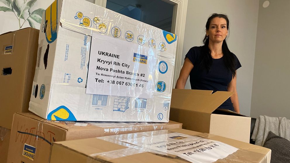 Bild på en svartklädd kvinna bredvid en låda där det står Ukraina. Lådan är från den ideella föreningen Ukrainas vänner som hjälper ukrainare i Uddevalla. Kvinnan på bilden heter Anneli Lillmaa och var med och startade föreningen.