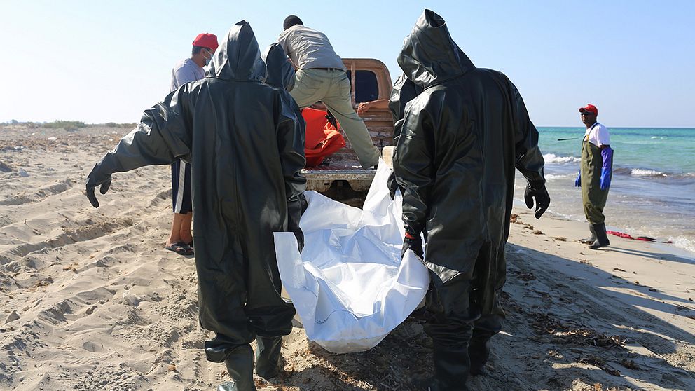 Hjälparbetare plockar upp döda kroppar på en strand i Libyen.