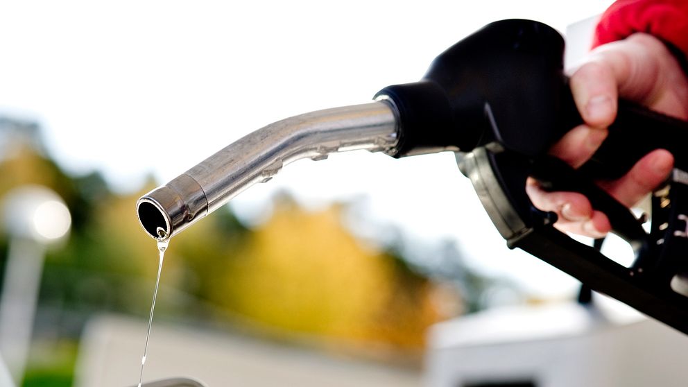 Närbild på munstycke till en bensinpump, och en hand som håller i pumphandtaget.