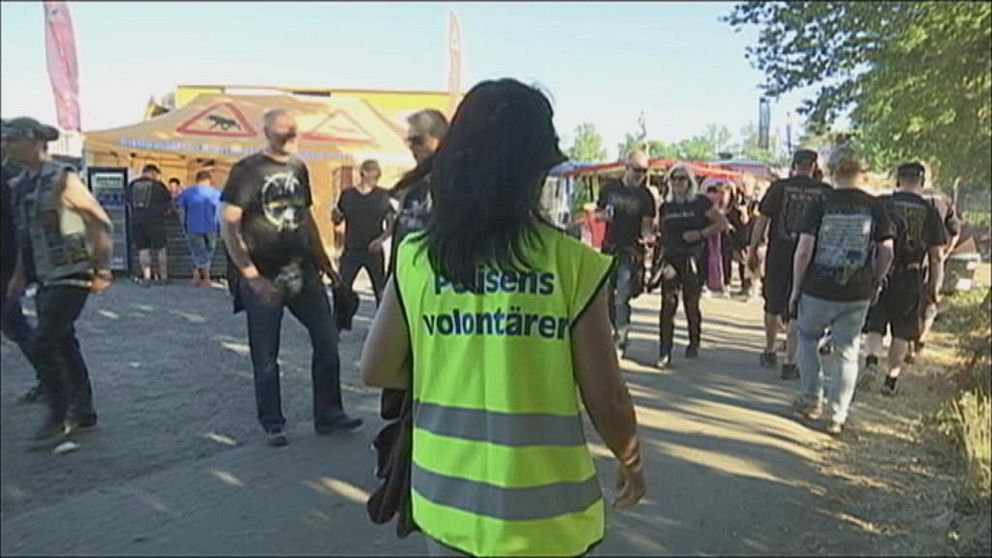 en person som visar ryggen och har en reflexväst på sig, där det står polisens volontärer. På ett evenemang med många människor runt om.