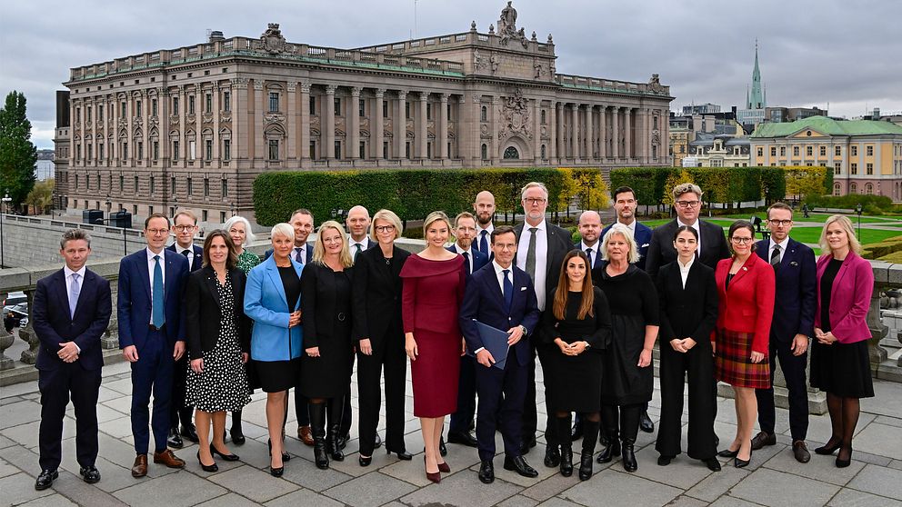 Sveriges ministrar uppställda med riksdagshuset i bakgrunden.