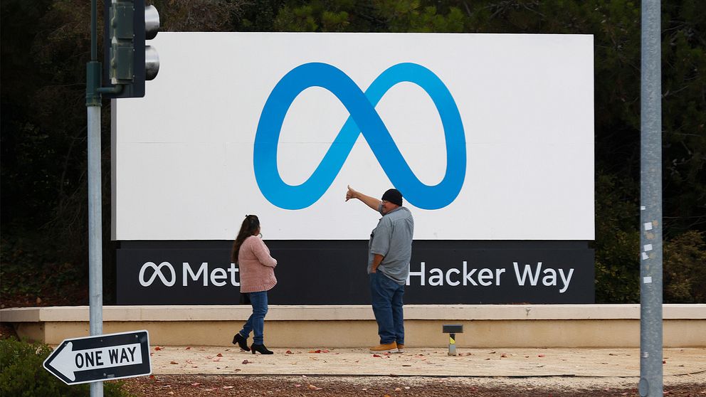 Bilden föreställer två människor som står framför Metas skylt vid huvudkontoret i Kalifornien.