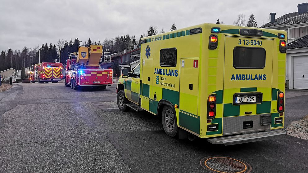 Bild på en gata där en ambulans syns bakifrån, framför står två brandbilar. Till höger ser man bland annat några villatak.