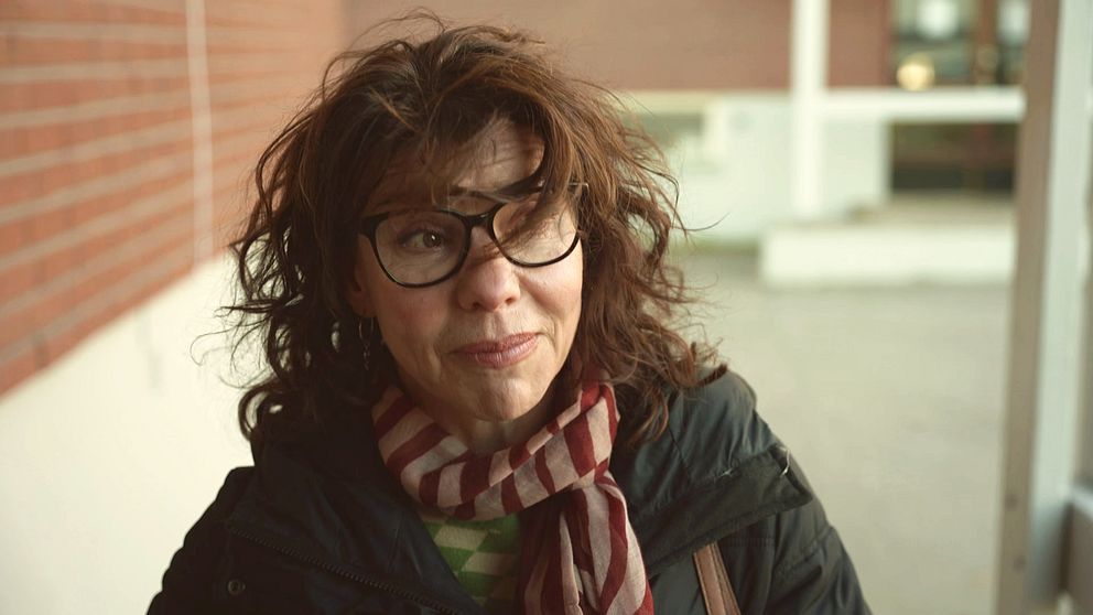 Gällivares kulturchef Anette Winblad intervjuas av SVT om bostadsbristen i Kiruna. Hon har lockigt brunt hår och svarta glasögon och står framför en tegelvägg. När hon flyttade till kommunen fick hon själv bo i en enrummare med delat kök och dusch.