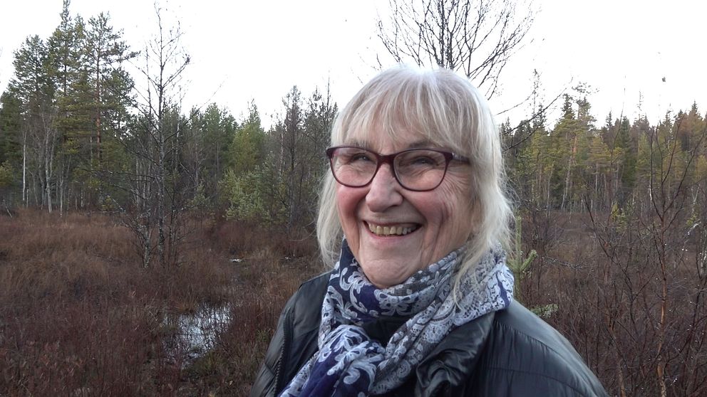 Birgitta Velander står i skogsmiljö. Hon har kort ljust hår och glasögon och ler mot kameran.