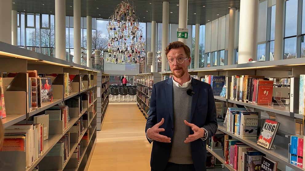 Bild på en man i kostym som står mellan två bokhyllor. Mannen är bibliotekschef Finn Axelsson och jobbar på Halmstads Stadsbibliotek som firar hundra år.
