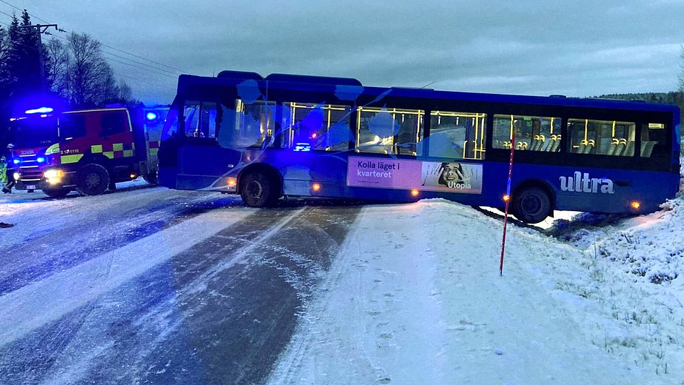 En blå buss står tvärsöver vägen. Räddningstjänsten syns i bakgrunden.
