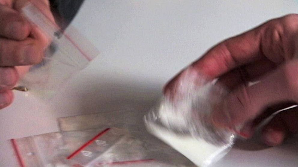Närbild på händer som håller i små plastpåsar med vitt pulverliknande innehåll som ska föreställa vara narkotika.