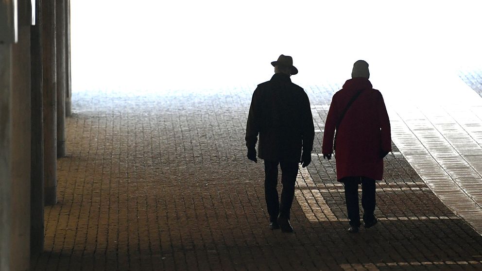 Två pensionärer på promenad vid Tegelbacken i Stockholm. Gubben till vänster bär hatt.