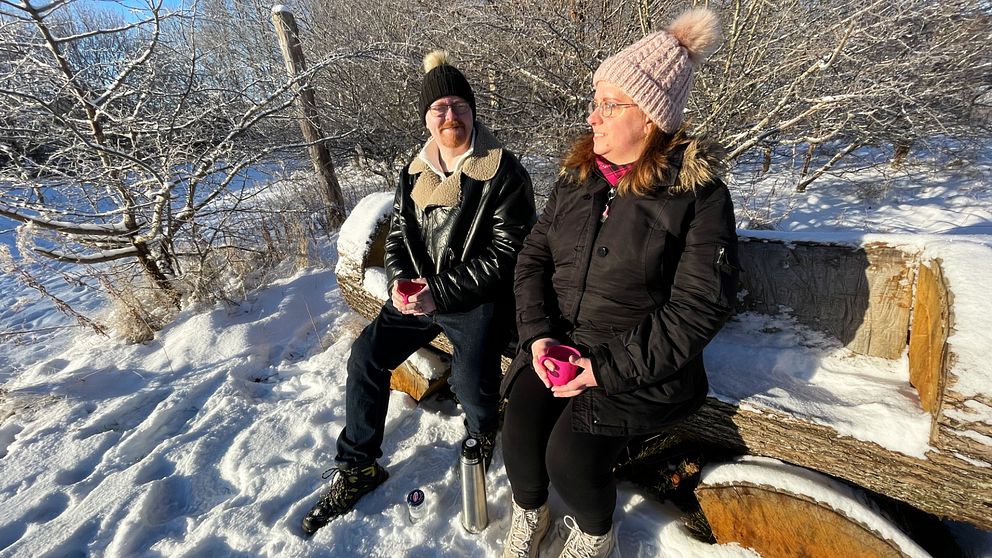 Två kvinnor sitter på en bänk i ett vinterlandskap med snö och sol.