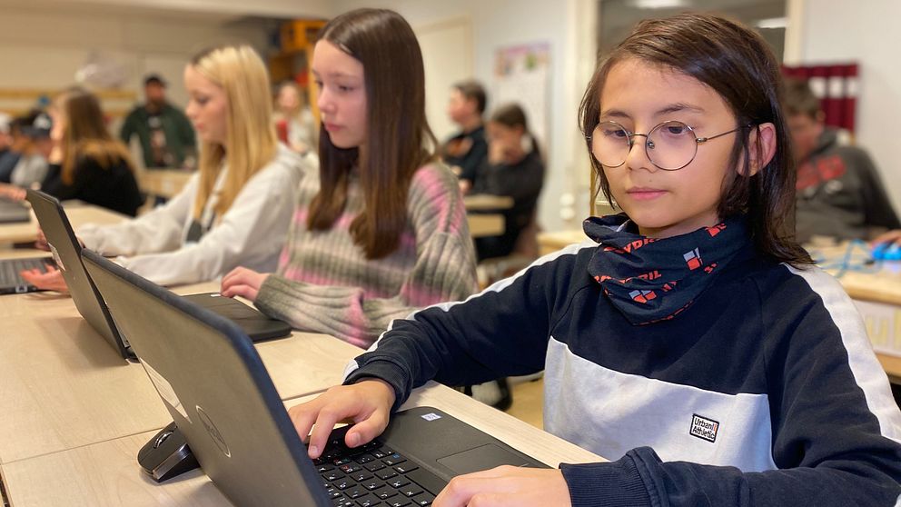 Vi befinner oss i ett klassrum där eleverna i årskurs sex på Ersmarksskolan sitter med sina datorer. Vi ser ett barn med mörkt axellångt hår och glasögon i förgrunden.