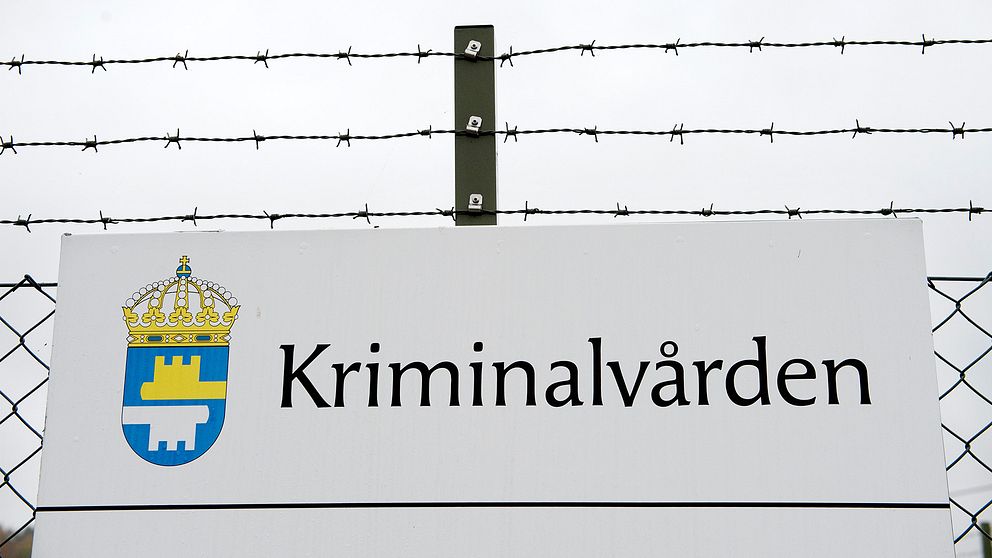 Exteriörbild på ett staket med Kriminalvårdens skylt.