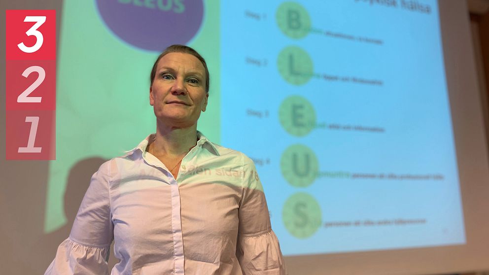 Kuraledare och universitetslektorn, Åsa Konradsson-Geuken, står framför en powerpoint bild som visar vilka steg man ska ta vid första hjälpen för att stödja en person som befinner sig i ett psykiskt kristillstånd – BLEUS är ordkombinationen som visas, hör vad de står för i klippet.