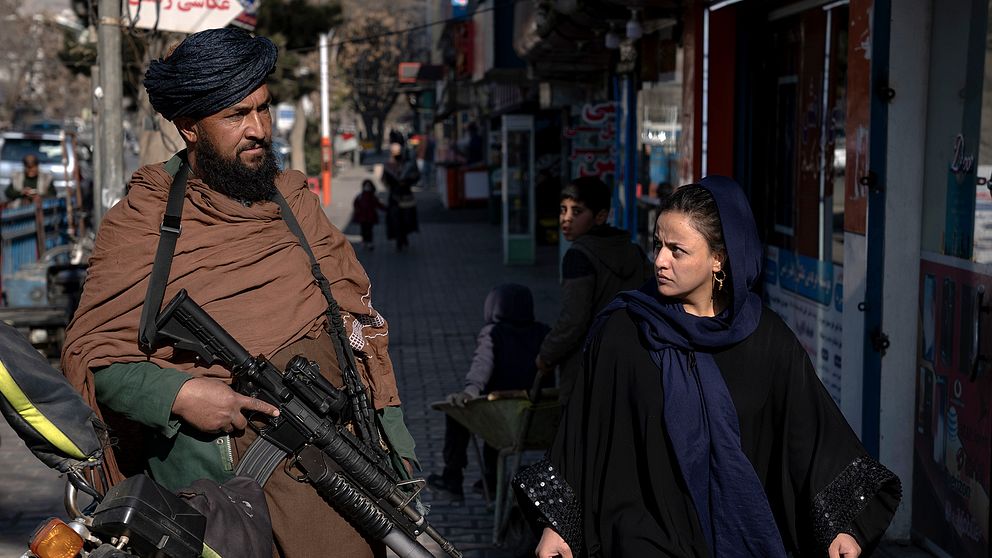 En talibankrigare med ett automatgevär passeras av en kvinna i centrala Kabul