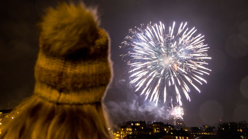 Bild på fyrverkeri, i förgrunden syns en flicka med mössa, fotograferad bakifrån.