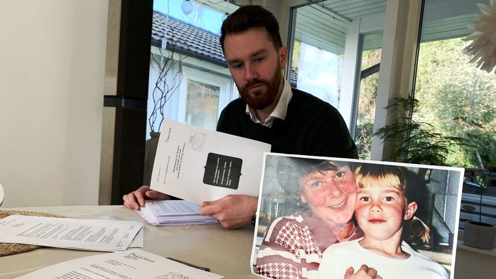 Bild på en man med skägg och skjorta som sitter med pappershögar och tittar på en bild på ett barn och en mamma. Mannen på bilden heter Niklas Holmquist i Kungsbacka som anmälde medicinkliniken i Halland efter att hans mamma dött.