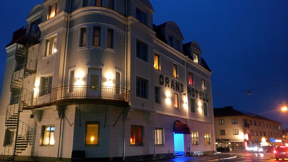 Grand hotell, i sin vita fasad, upplyst av flera vägglampor på bild tagen i kvällsmörker.