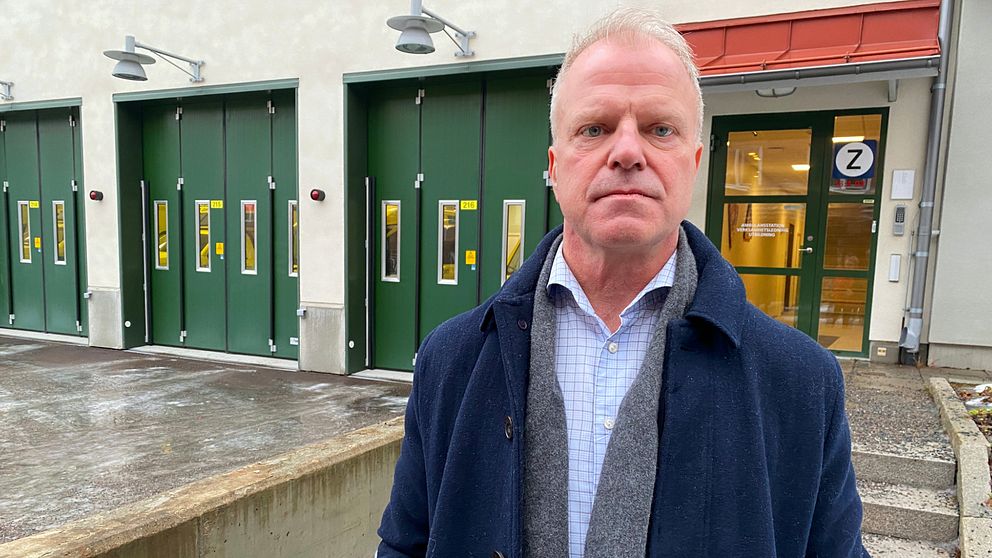 Fredrik Forselius, som är ambulanschef vid Region Dalarna och bär en blå rock, står framför ett ambulansgarage med gröna portar och berättar om det svåra personalläget.