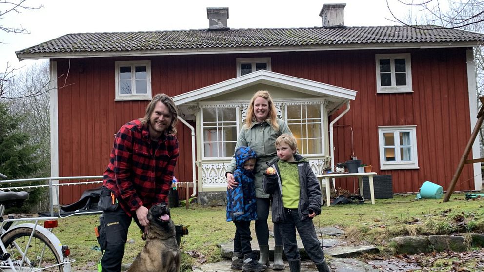 Bild på en man, en kvinna och, två barn och en hund som står framför ett rött hus med vita knutar. Det är pappa Geert och mamma Lynn tillsammans med barnen Thyten och Yzeron samt hunden Luna, som står framför det obebodda fritidshus som familjen köpte i september 2022.