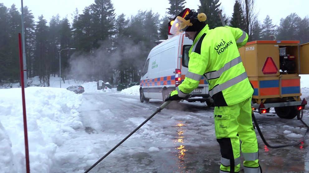Man med varselkläder som står med ett verktyg som används för att tina upp brunnar. Det är vinter och snö. Bakom honom står en skåpbil från Umeå kommun.