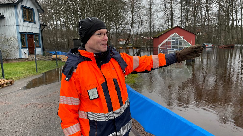 En man i skyddskläder pekar ut mot ett översvämmat område.