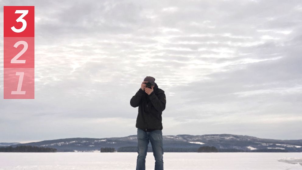 En man står i ett snölandskap och fotograferar med en kamera.