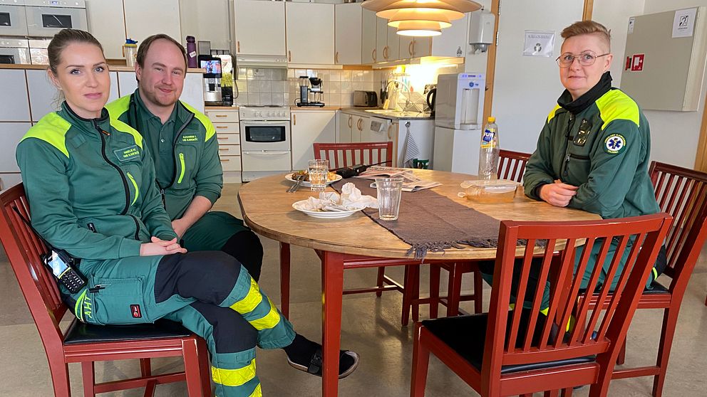 Ambulanspersonal vid lunchbord som tittar in i kameran