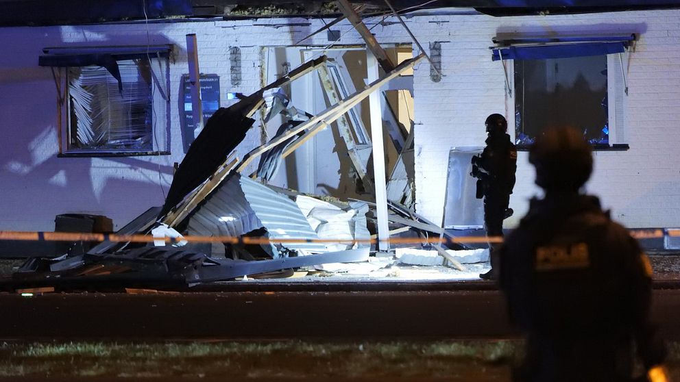 Entrén till en byggnad skadad av en explosion på Råå i Helsingborg. Beväpnad polis bevakar.