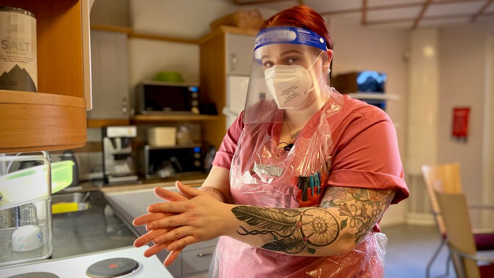 Emma Fjellner står i ett kök i full skyddsutrustning och smörjer in händerna med alkogel.